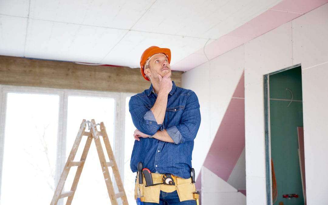 Portrait of thinking handyman standing with hand on his chin at the construction site.